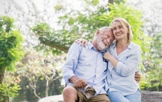 Happy senior couple sitting on a rock outside smiling