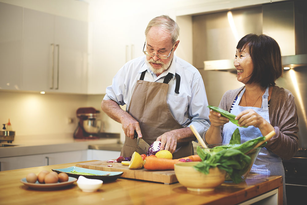 Senior couple making a healthy meal with veggies in kitchen