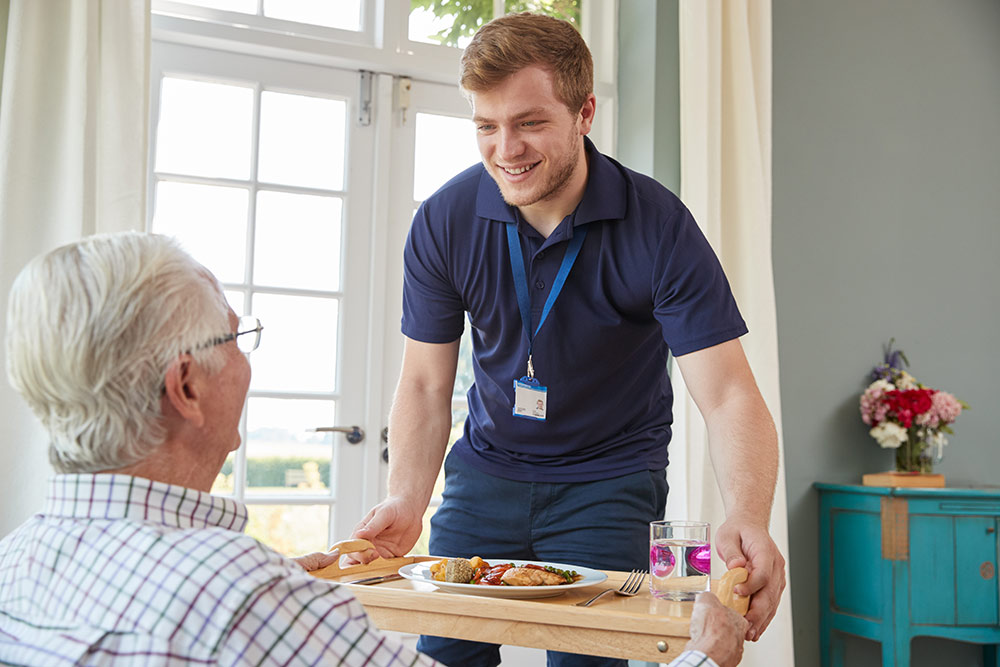 senior man with caregiver receiving meal in dementia care assisted living