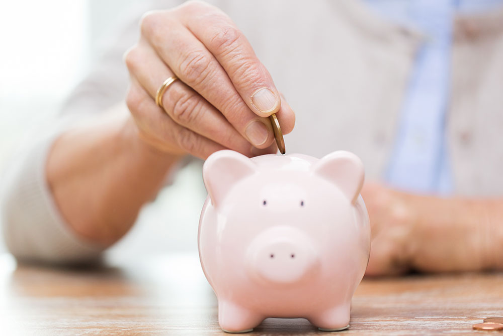 Close up of senior putting money in piggy bank, saving money for retirement