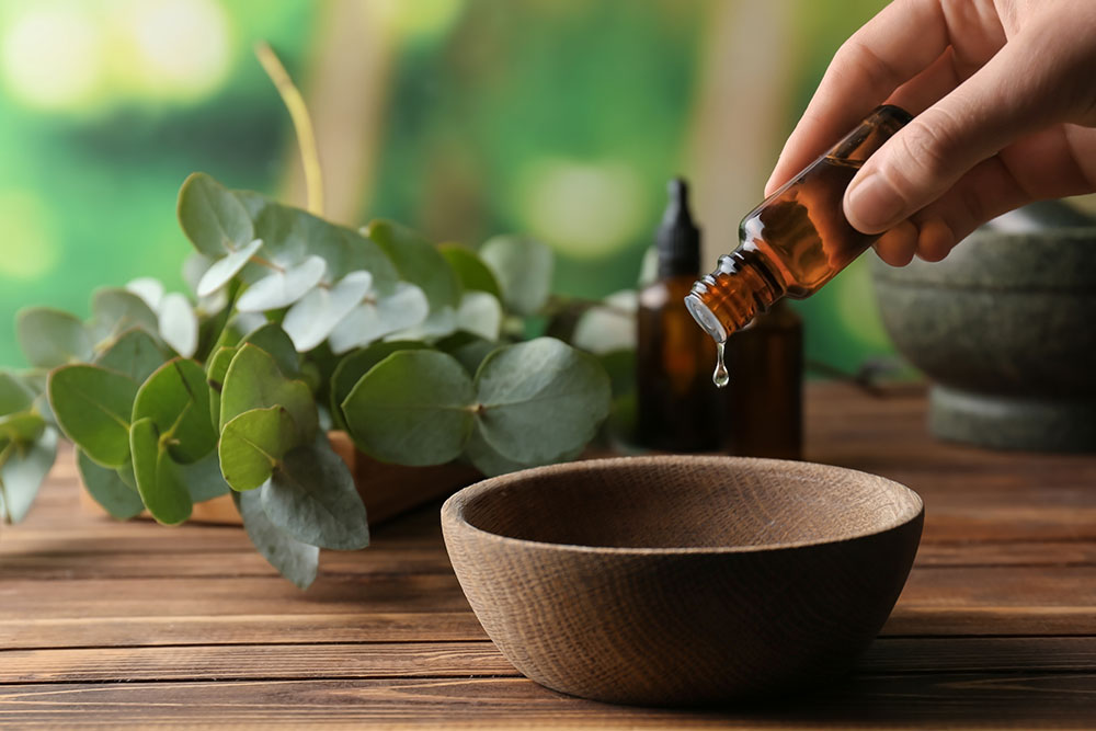 Hand dropping essential oils into bowl on table