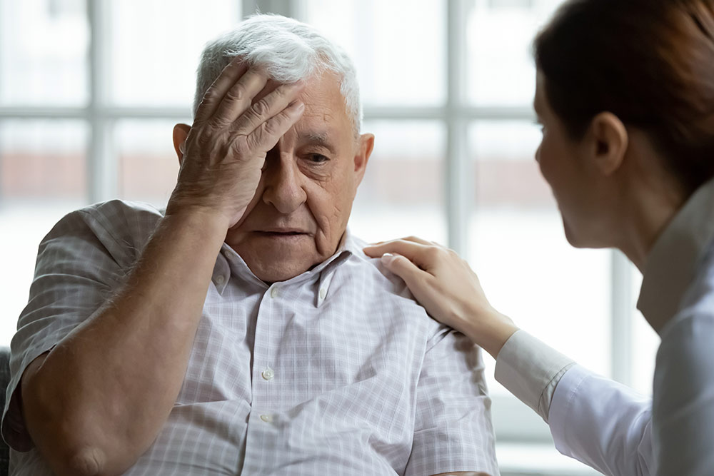 Senior man with dementia holding head, forgetful, memory loss, with caregiver