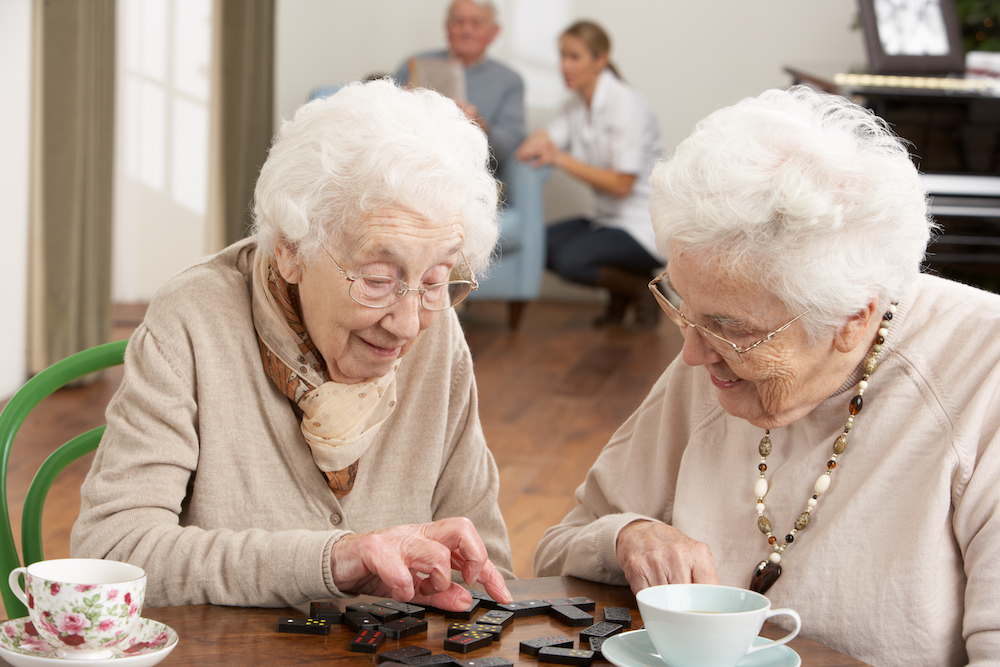 Two senior women play dominos at a senior living center.