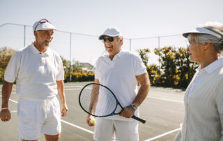 Three seniors play tennis together outdoors