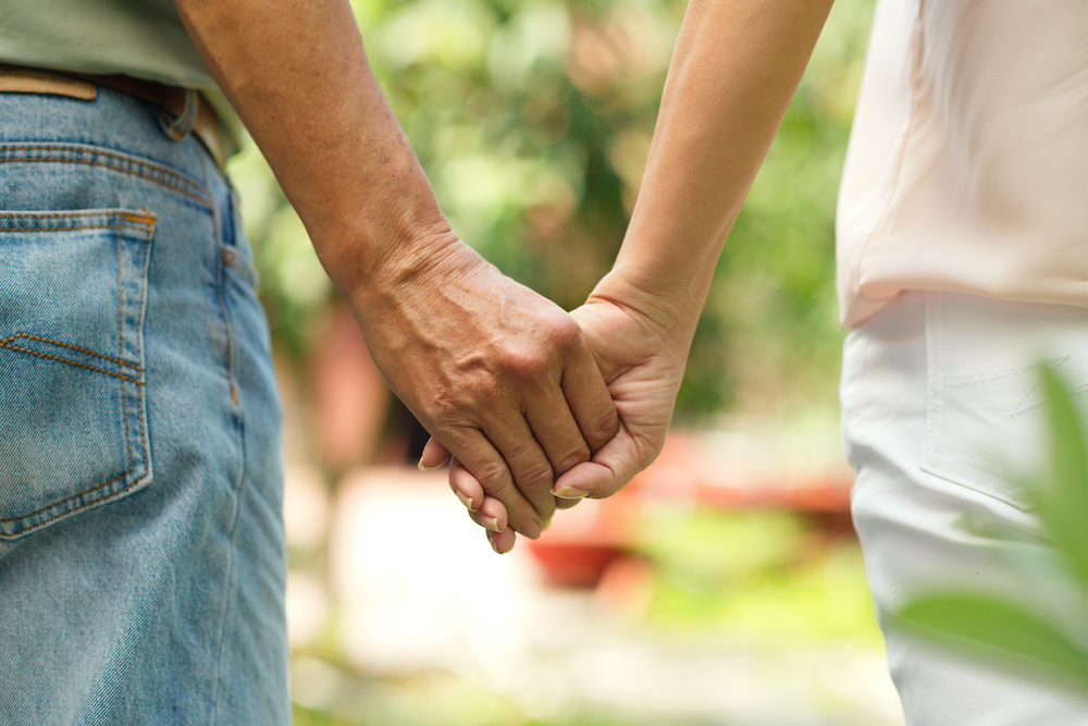 A senior man holds hands with a caregiver