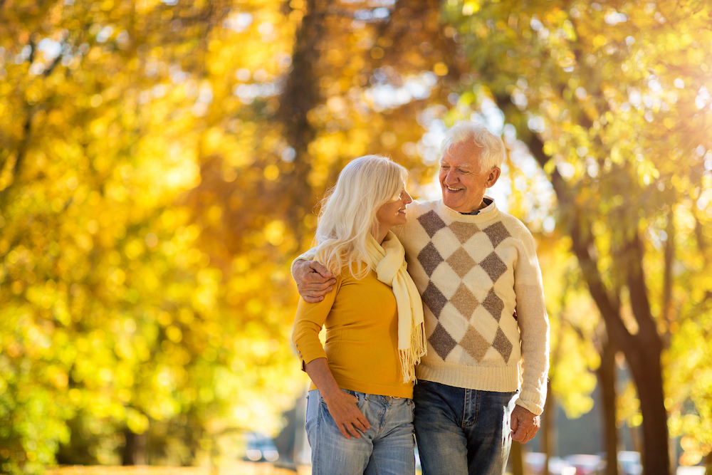 A senior couple at senior living goes for a fall walk outdoors at a park