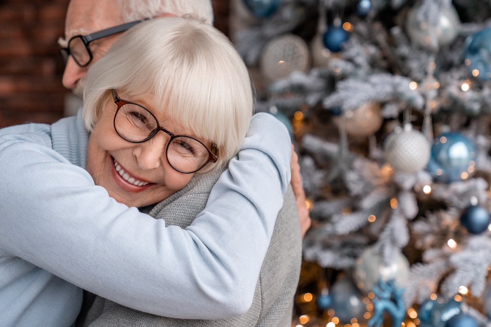 A senior couple hugs in front of a Christmas tree