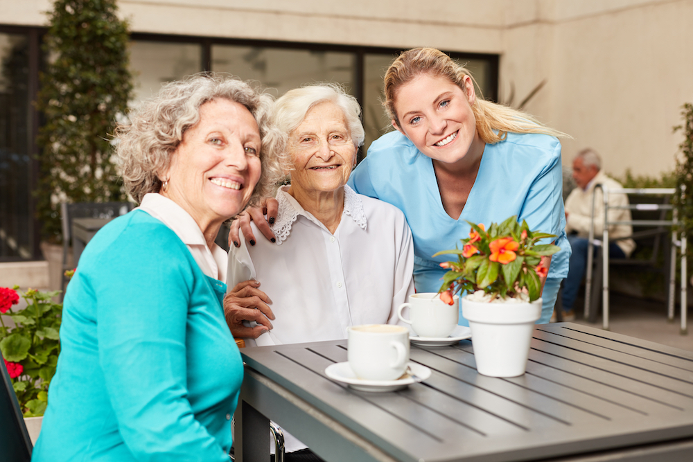 A senior woman and her daughter drinking coffee on the patio with a caregiver from Palm Springs memory care