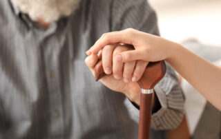 A senior man holding hands with a caregiver over his cane
