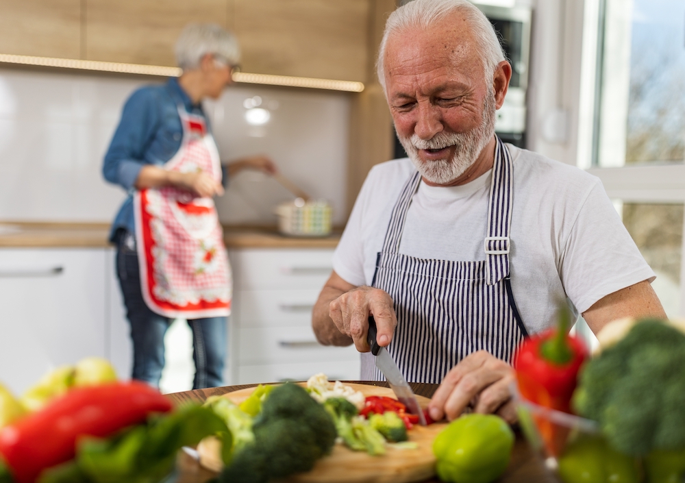 A senior man cuts up vegetables for dinner while cooking