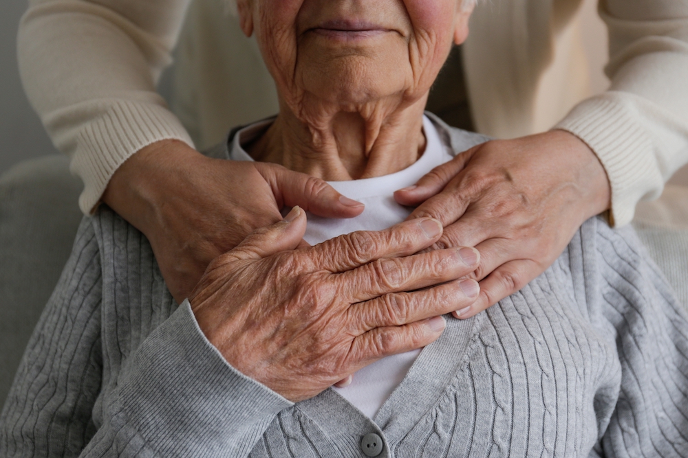 An adult daughter rests her hands on top of her senior mother's