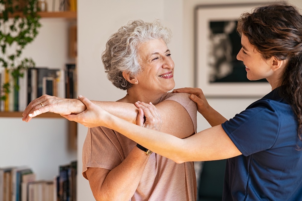 A caregiver helpinng a senior woman do her stretches