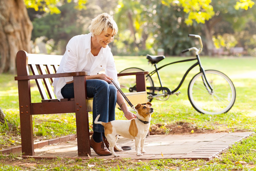 A happy senior woman walks her dog outdoors through a park